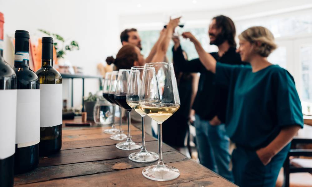 A group of men and women cheers with an array of glasses and bottles filled with red and white wine for a wine tasting.